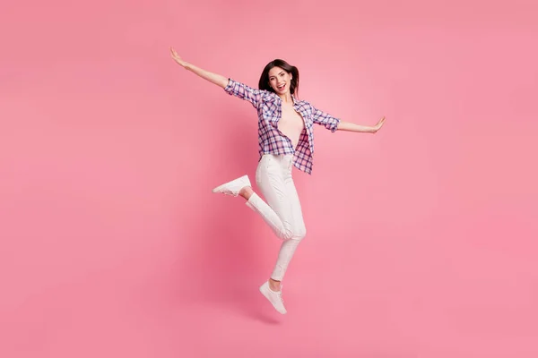フルレングスのサイドプロファイルボディサイズの写真美人彼女彼女の女性ジャンプ高いふり空気飛行架空の翼は、靴カジュアルチェッカー格子シャツホワイトジーンズデニムの服孤立したピンクの背景 — ストック写真