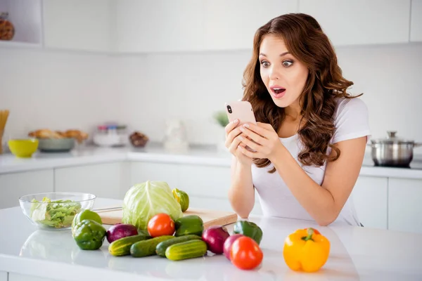 Portrait of her she nice-looking attractive lovely wondered stunned astonished wavy-haired girl reading recipe online fresh lunch dinner farm organic vegs in light white interior room