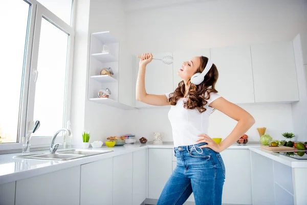 Perfil vista lateral retrato dela ela agradável atraente adorável adorável alegre alegre menina de cabelos ondulados segurando na mão utensílios de cozinha como som de microfone pop na luz moderna sala de estilo interior branco — Fotografia de Stock