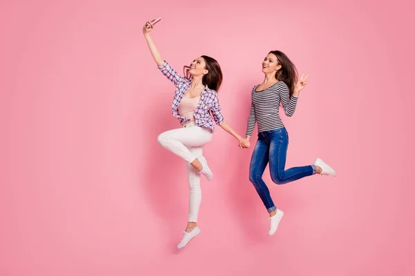 Volledige lengte lichaam grootte foto vrolijke positieve studenten meisjes hebben video-oproep stijlvolle bloggers vrije tijd weekend vakantie Greet make show v-Signs gekleed moderne shirts jeans geïsoleerde roze achtergrond — Stockfoto