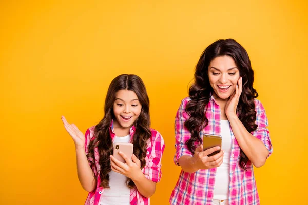 De cerca foto hermosa madre de pelo castaño pequeña hija teléfono inteligente lector de teléfonos oh sí sí sms buena noticia información desgaste casual rosa cuadros camisas aisladas fondo amarillo —  Fotos de Stock