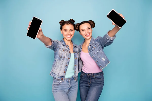 Retrato de lindos adolescentes atractivos adictos a la tecnología moderna cogidos de la mano tienen paseos muestran gadgets dan retroalimentación recomiendan aconsejan fondo azul aislado vestido ropa de mezclilla —  Fotos de Stock