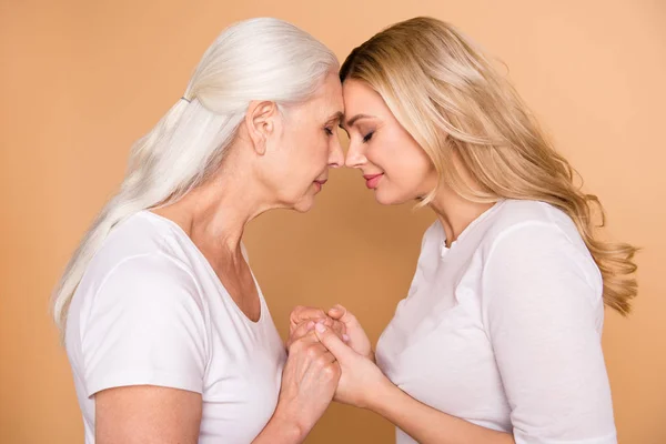 Close-up profile side view portrait of nice-looking winsome sweet attractive charming dreamy ladies wearing white outfit holding hands support care generation isolated over beige pastel background — Stock Photo, Image