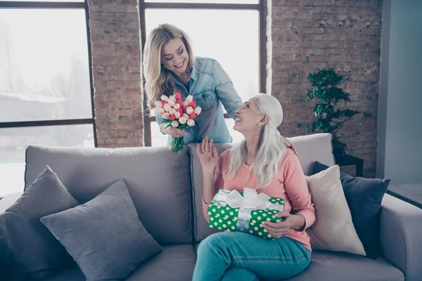 Närbild foto två personer hon hennes damer barn mormor barnbarn besök födelsedags fest leverera mamma giftbox färska blommor casual inhemska kläder sitta bekväm soffa Divan platt hus inomhus — Stockfoto