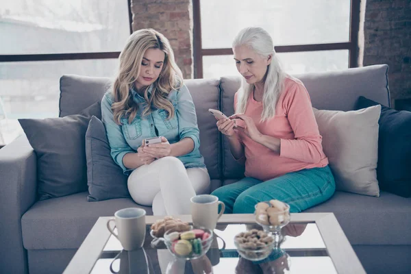 Крупним планом дві красиві жінки бабуся бабуся родичі мама тримає руки руки руки смартфон, не зацікавлений у розмові сидіти диван диван будинок в приміщенні — стокове фото