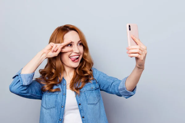 Close up photo beautiful amazing she her curly foxy lady show v-sign tongue out mouth hold arm hand phone make take selfies pictures wear casual blue jeans denim shirt isolated grey background —  Fotos de Stock