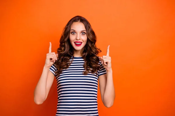 Close up foto bonita ela sua senhora brilho lábios vermelhos encaracolado longo penteado indicar dedos para cima espaço vazio aconselhando novidade desgaste casual listrado branco azul t-shirt roupas isolado laranja brilhante fundo — Fotografia de Stock