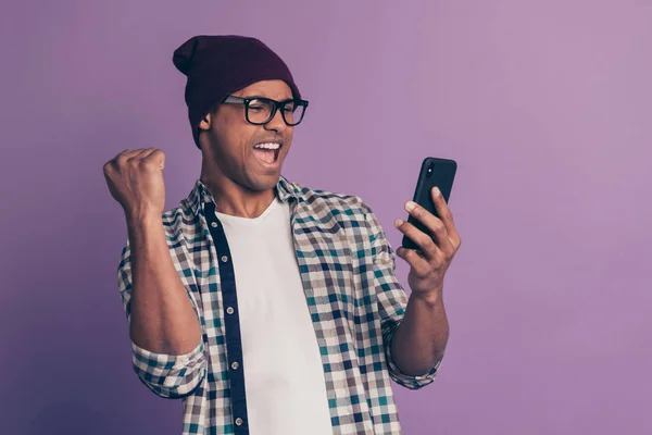 Hooray yeah Photo of cool modern positive cheerful delightful ecstatic blogger student raising fist using holding gadget smart device in hand read notification isolated violet background