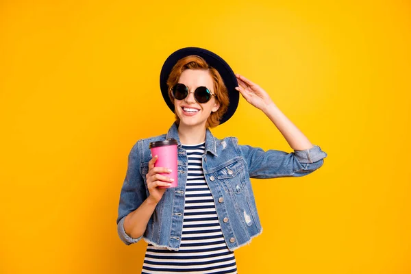 Close up photo beautiful she her lady traveler modern perfect look hand pink coffee container wear specs vintage hat casual striped t-shirt jacket jeans denim isolated yellow background — стоковое фото