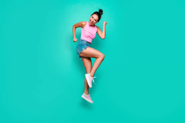 Full length side profile body size photo beautiful she her trendy hairdo jump high yell scream shout yeah wild roar wear casual pink tank-top jeans denim shorts isolated teal turquoise background