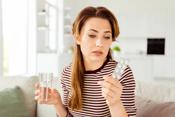 Close up photo of serious lady contemplate discomfort hurt injury hold medicine pills cure virus allergy inflammation have striped shirt long curly wavy hair wear sit divan in light apartment — Stock Photo, Image