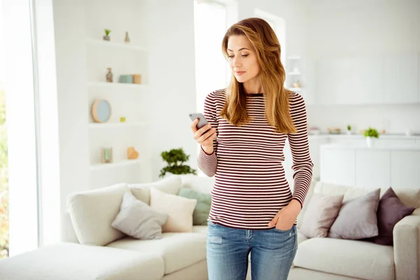 Portret positieve mooie aantrekkelijke student Hold apparaat moderne technologiegebruikers apps gebruiken zoek informatie Communiceer draadloze verbinding krullend golvend haar kapsel gestreepte shirt denim kleding kamer — Stockfoto