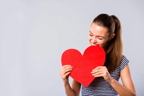 Close up photo beautiful amazing she her lady hold hands arms big large red paper heart shape figure postcard bite it laughter game play wear blue white striped t-shirt isolated grey background — Stock Photo, Image