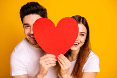 Close up photo beautiful she her he him his guy lady hiding facial expression laugh laughter hold hands arms heart shape paper postcard in love wear casual white t-shirts isolated yellow background clipart