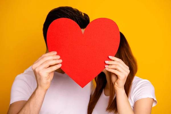Close up photo beautiful she her he him his guy lady hiding kissing faces hold hands arms big heart shape paper postcard best emotions in love wear casual white t-shirts isolated yellow background — Stock Photo, Image