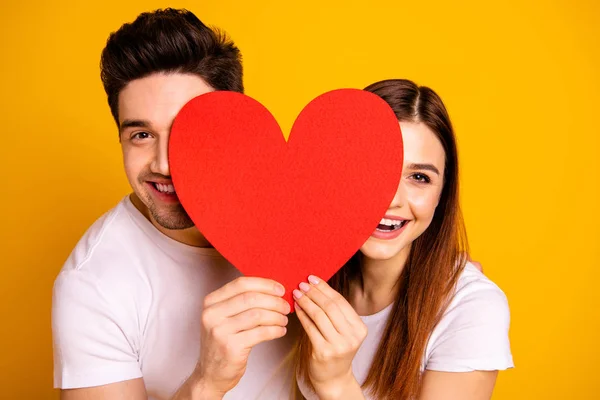 Close up photo beautiful she her he him his guy lady hiding facial expression laugh laughter hold hands arms heart shape paper postcard in love wear casual white t-shirts isolated yellow background — Stock Photo, Image
