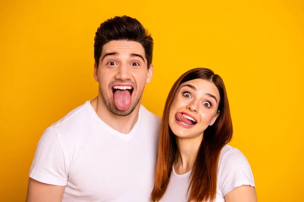 Close up photo beautiful amazing she her he him his guy lady pair tongue out mouth  careless funny funky foolish making stupid facial expressions wear casual white t-shirts isolated yellow background — Stock Photo, Image