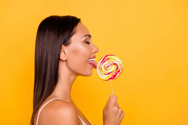 Close up side profile photo beautiful she her lady hungry addicted sweets person big lolly pop wooden stick licking overjoyed eyes closed wear casual pastel tank-top isolated yellow bright background — Stock Photo, Image