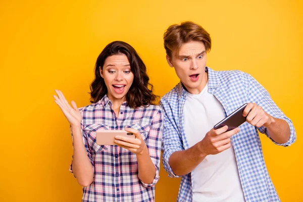 Close up foto di coppia adolescenti lui la sua lei il suo ragazzo signora con telefoni in armi grande vittoria e grande perdere indossare casual camicie a quadri vestito isolato su sfondo arancione giallo — Foto Stock