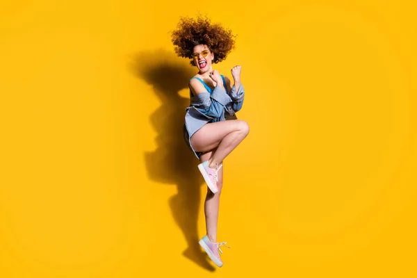 フルレングスサイドプロファイルボディサイズ写真面白いファンキー彼女彼女の女性波状のスタイリングカールジャンプハイグレートウィンウェアスペックカジュアルジーンズデニムシャツショートパンツタンクトップ服孤立黄色明るい背景 — ストック写真