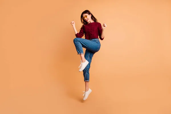 Повна довжина бічного профілю кузова фото красива її леді стрибає високі руки кулаки підняті зношені специфікації повсякденні джинси джинси червоний бордовий в'язаний пуловер ізольований пастельно-бежевий фон — стокове фото