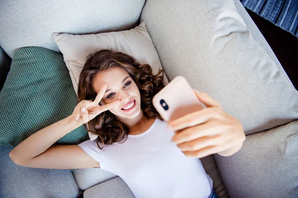 Topo acima de ângulo alto vista retrato dela ela agradável-olhando atraente lindo brilho adorável doce alegre alegre menina de cabelos ondulados deitado no divã tirar selfie mostrando v-sinal dentro de casa — Fotografia de Stock