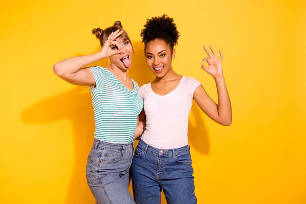 Close-up foto funky mooi ze haar dame knuffel omarmen knuffelen verschillende vrienden houden handen armen okey symbool tong uit mond slijtage casual wit gestreepte t-shirt outfit geïsoleerd gele lichte achtergrond — Stockfoto