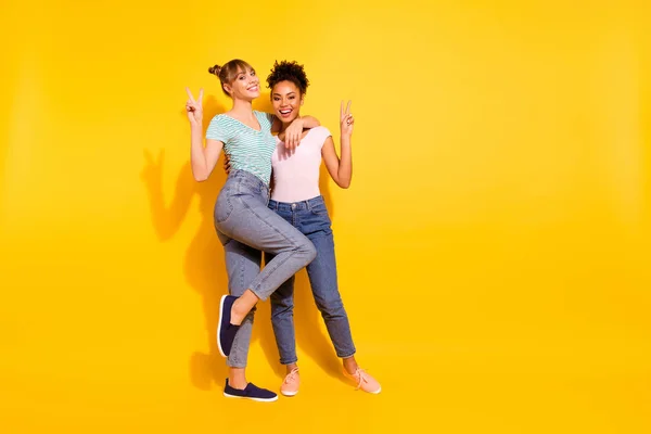 Volledige lengte lichaam grootte foto mooi ze haar Lady beste maatjes verschillende nationaliteiten Hold handen armen v-teken zeggen hallo hallo dragen casual wit gestreepte t-shirt kleren outfit geïsoleerd gele achtergrond — Stockfoto