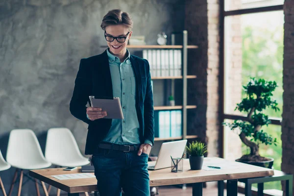 Retrato de contenido alegre positivo hombre smm disfrutar emocionado satisfecho gafas gafas gafas navegar por Internet en línea celebrar noticias dispositivo de la mano leer traje elegante moderno stand interior industrial —  Fotos de Stock