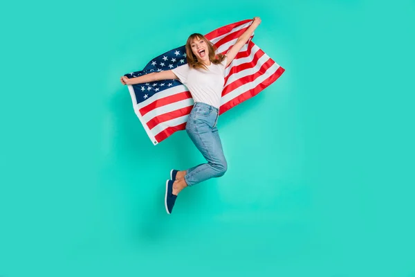 Full length side profile body size photo beautiful she her lady jump high arms hands hold american flag festive crazy carefree patriot wear specs casual white t-shirt isolated teal green background