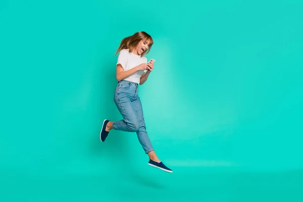 Full length side profile body size photo beautiful she her lady weekend vacation jump high arms hands hold telephone smart phone achieve wear casual jeans jeans branco t-shirt isolado teal background — Fotografia de Stock