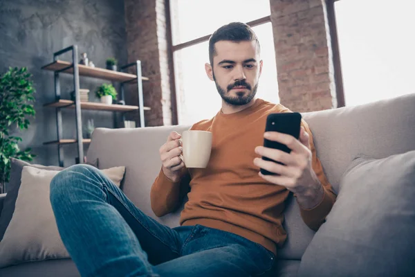 Bajo por debajo del ángulo ver retrato de su él atractivo contenido seguro freelancer barbudo chico bebiendo café con leche escritura sms en el loft industrial ladrillo estilo interior sala de estar — Foto de Stock