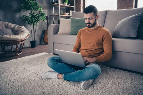 Porträtt av koncentrerad fokuserad man ungdom Sit Lotus position titta Läs data statistik hantering denim jeans orange Pullover tröja stora ljus interiör — Stockfoto