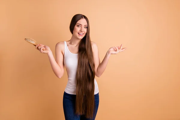 Close up foto bonita ela ela ela braços senhora mãos escova de cabelo apresentando cabelos castanhos muito longos grande condição cachos resultado use desgaste casual branco-top jeans jeans isolado pastel bege fundo — Fotografia de Stock