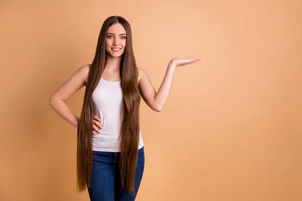 Close-up foto mooi haar She Lady zeer lang bruin haar open arm hand lege ruimte aanbevelen kopen koper nieuwe snit styling balsem slijtage casual Tank-Top jeans geïsoleerd pastel beige achtergrond — Stockfoto