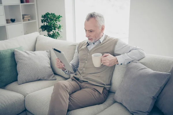 Close up side profile photo amazing he him his aged man hands arms hot beverage e-reader information book adventure novel wear white shirt waistcoat pants sit cozy divan flat house living room indoors — Stock Photo, Image