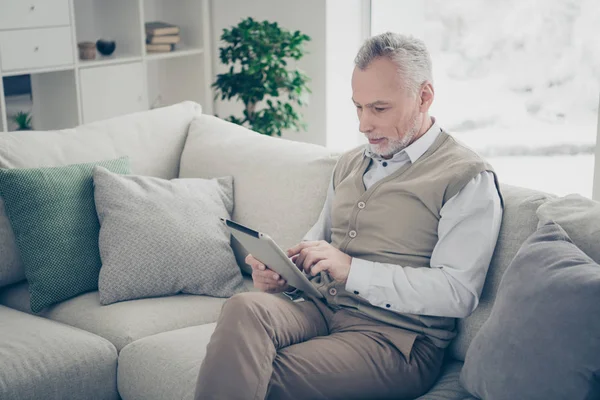 Close up side profile photo amazing he him his aged man hands arms e-book search look browsing information novelty wear white shirt waistcoat pants sit cozy divan flat house living room indoors — Stock Photo, Image