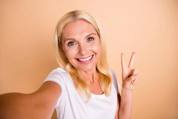 Primeros planos foto de adorable dama hacer tomar selfies v-signo símbolo decir hola hola desgaste blanco casual camiseta aislado pastel beige fondo —  Fotos de Stock