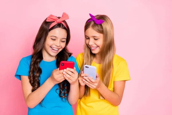 Retrato de niños alegres riendo mantenga gadgets mirada información divertida desgaste tendencias típicamente camisetas diademas aisladas sobre fondo rosa —  Fotos de Stock