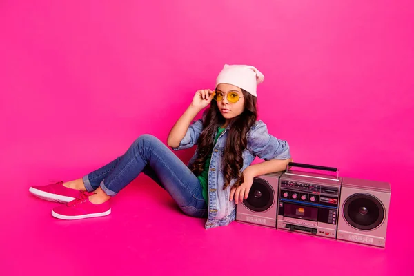 Full length side profile body size photo beautiful little she her curly brunette lady sit old-fashioned tape audio recorder wear yellow sun specs hat casual jeans denim jacket isolated pink background