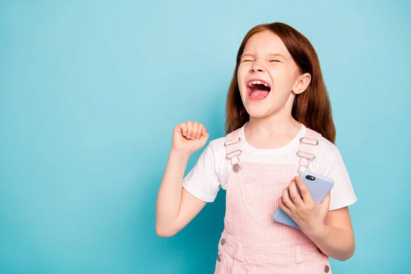 Close up foto de criança encantada levantar as mãos gritar sim fechar os olhos têm dispositivo usar macacão elegante moda isolado fundo azul — Fotografia de Stock