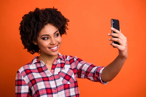 Zavři fotku hezkých paní, podrž si ruce telefon dělat, jak si na sebe obléct příležitostnou šachovnou košili izolované oranžové pozadí — Stock fotografie