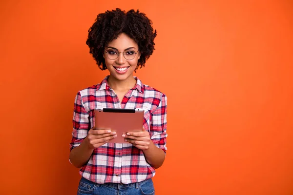 Porträt von netten netten attraktiven schönen fröhlich fröhlich smart kluge wellige Dame Nerd tragen kariertes Hemd hält in den Händen digitales E-Book isoliert über hellen lebendigen Glanz orange Hintergrund — Stockfoto