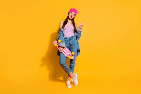 Full length dimensioni del corpo foto bella lei la sua signora incredibile bello sguardo mano braccio skate board pericoloso sport v-segno simbolo indossare jeans casual giacca di jeans scarpe rosa cappello isolato giallo vivido sfondo — Foto Stock