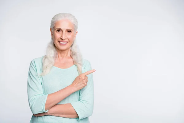 Retrato de una encantadora anciana apuntando al espacio de copia mostrando anuncios promocionales con jersey de color verde azulado aislado sobre fondo blanco —  Fotos de Stock