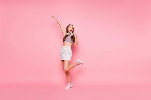 Full size photo of carefree lady with close eyes raising hand leg wearing white denim jeans skirt grey tank-top isolated over pink background — Stock Photo, Image