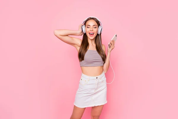 Retrato de hermosa juventud con los ojos cerrados sosteniendo la tecnología moderna con pantalones vaqueros falda blanca camiseta gris aislada sobre fondo rosa — Foto de Stock