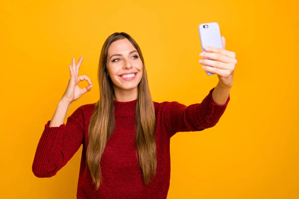 Bonita dama sosteniendo manos telefónicas haciendo selfies mostrando okey símbolo desgaste jersey de punto aislado fondo amarillo —  Fotos de Stock