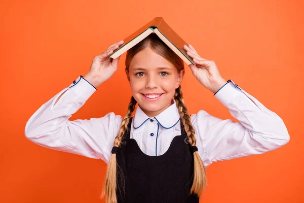 Portrétní portrét její bystré a příjemné veselé dospívající dívky, které drží nad hlavou akademickou knížku první 1. září se izolovala přes zářivě svěží oranžové pozadí — Stock fotografie