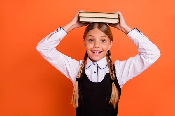 Close-up portret van haar ze mooie aantrekkelijke mooie charmante schattige vrolijke vrolijke speelse pre-tiener meisje houden op hoofd boek klas cursus geïsoleerd over heldere levendige glans oranje achtergrond — Stockfoto